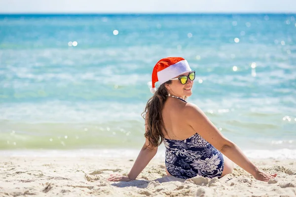 Jovem mulher em santa chapéu sentado na praia . — Fotografia de Stock