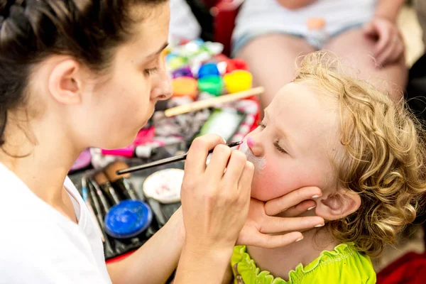 woman painting face of kid outdoors