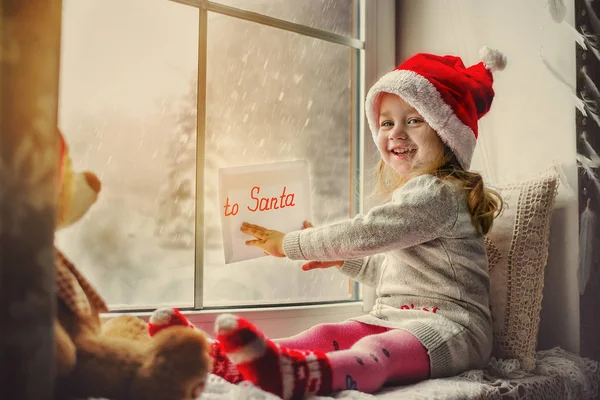 Jolie petite fille assise près de la fenêtre avec une lettre au Père Noël — Photo