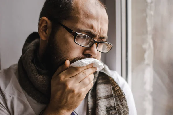 Junger Mann pustet sich die Nase aus, während er am Fenster sitzt — Stockfoto