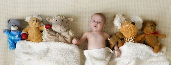 Menino feliz deitado com muitos brinquedos de pelúcia sob o cobertor — Fotografia de Stock