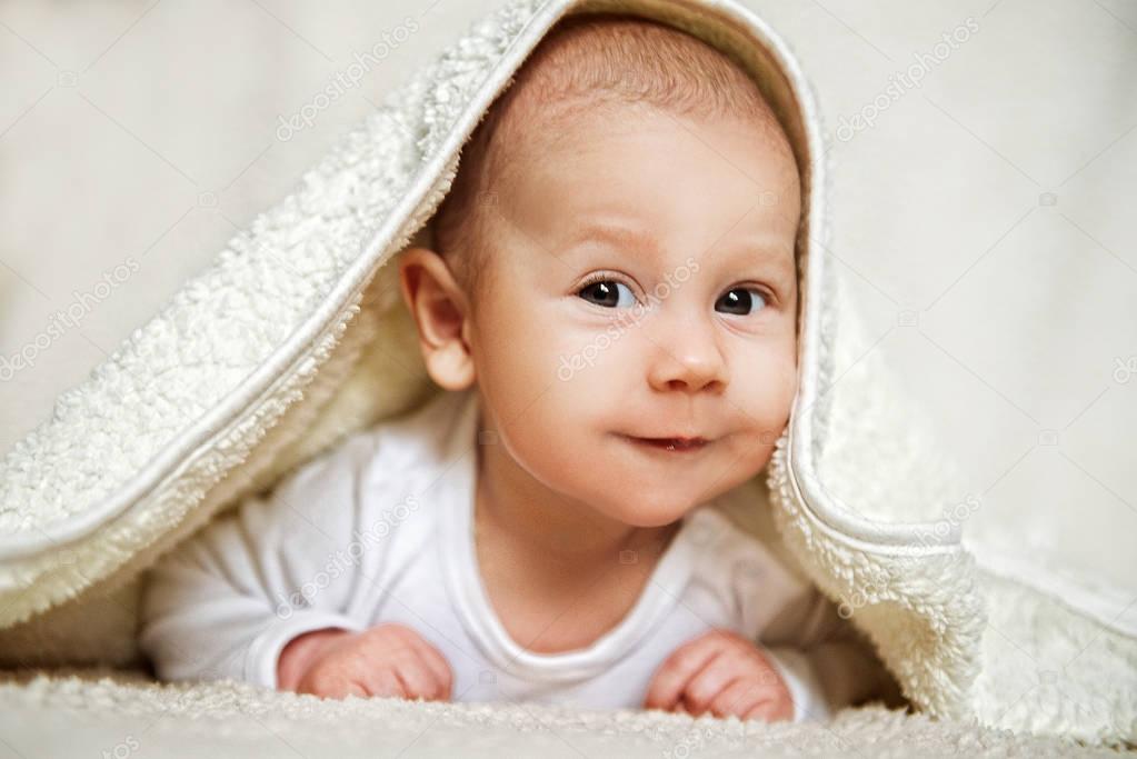 Portrait of a cute happy smiling 3 month old baby, boy or girl, peeking up from a white towel.