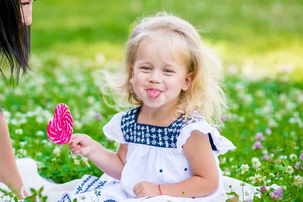快乐的小女孩，在一根棍子的心形式上吃一块糖. — 图库照片