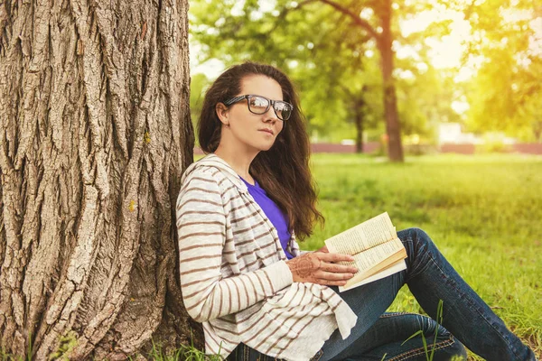 Bonito jovem mulher sentada na grama e lendo o livro — Fotografia de Stock