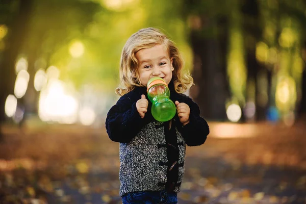 Niña linda bebiendo de la botella afuera en el parque —  Fotos de Stock