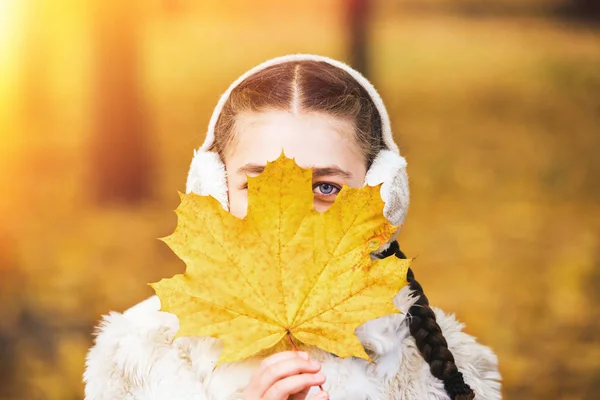 La niña está cubierta con una hoja de arce en el parque en otoño — Foto de Stock