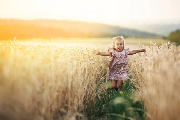 Glad springande flicka på ett vetefält i solljuset — Stockfoto