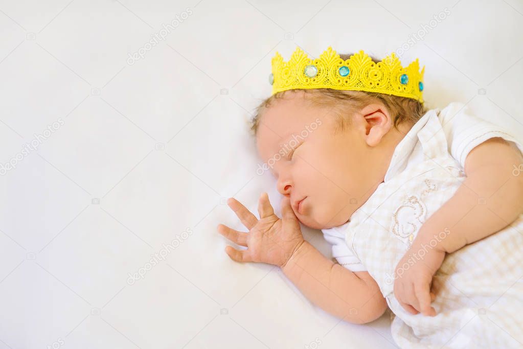 Portrait of a 12 day old newborn baby boy wearing a gold crown. He is sleeping on a beige flokati rug with his hands behind his head.
