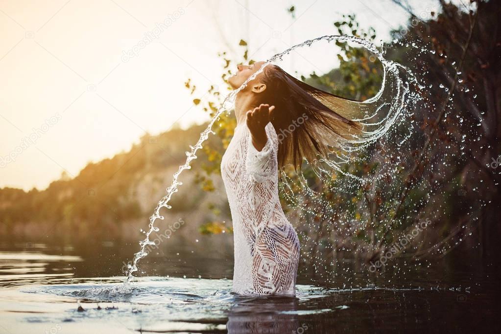 Beauty Model Girl Splashing Water with her Hair. Teen girl Swimming and splashing on summer beach.