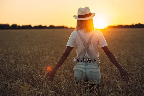 Junges Mädchen mit ausgebreiteten Händen steht bei Sonnenuntergang im Weizenfeld — Stockfoto