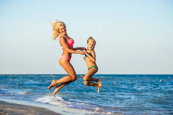 Retrato de acción de madre joven con hija saltando juntos en la playa. Chicas riendo en traje de baño — Foto de Stock