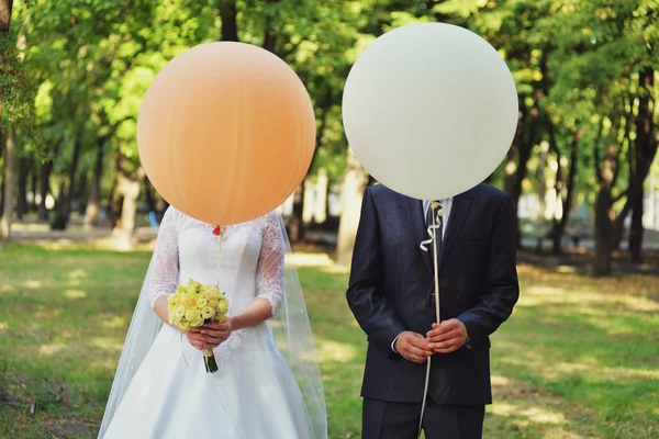 オレンジと白の風船で新婚夫婦。新婚夫婦と面白い写真。若いカップルは、大きなオレンジ色と白の風船で顔を覆われています。. — ストック写真