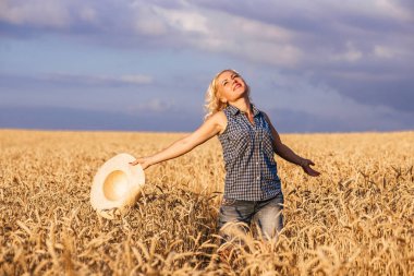 Güneşli bir günde, bir kadın bir doğa arka planda kavramı yaşam tarzı ekoloji çevre mutlu insanlar özgürlük, harika manzarasına hasır şapkalı beyaz bir elbise ile bir buğday alanı boyunca yürüyüş
