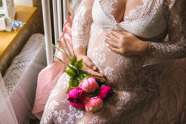 Close-up van een zwangere vrouw buik met een boeket bloemen. Zwangerschap, het concept van ouderschap, voorbereiding en verwachting. — Stockfoto
