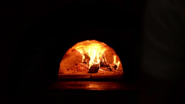 Tracking shot of unidentified cook placing pizza in wood-fired stove with pizza peel — Stock Video
