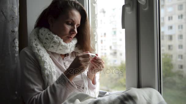 Een vrouw is ziek, dat ze meet de temperatuur van het lichaam, bij het raam — Stockvideo