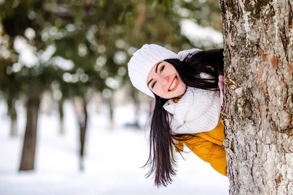 Retrato de menina bonita na neve escondida atrás de uma árvore . — Fotografia de Stock