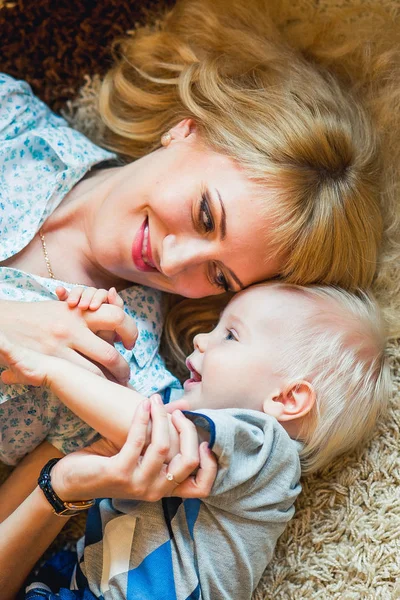 Draufsicht der schönen Frau und ihres niedlichen kleinen Sohnes, die auf dem Boden liegend in die Kamera schauen und lächeln — Stockfoto