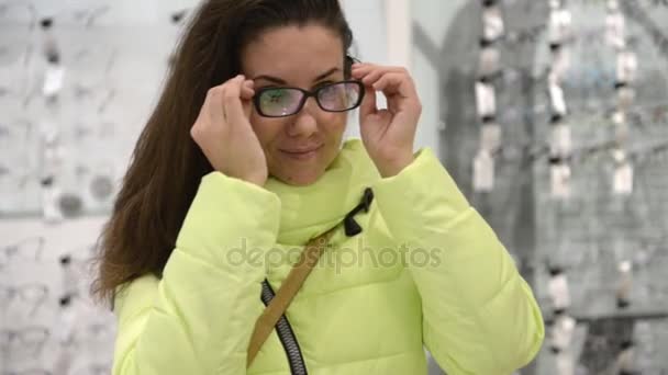 La chica está midiendo las gafas en la tienda. La chica se dedica a ir de compras — Vídeos de Stock