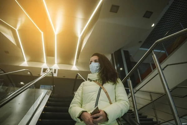 Persona que lleva máscara protectora contra enfermedades infecciosas transmisibles y como protección contra la contaminación y la gripe. Mujer en un centro comercial en una escalera mecánica — Foto de Stock