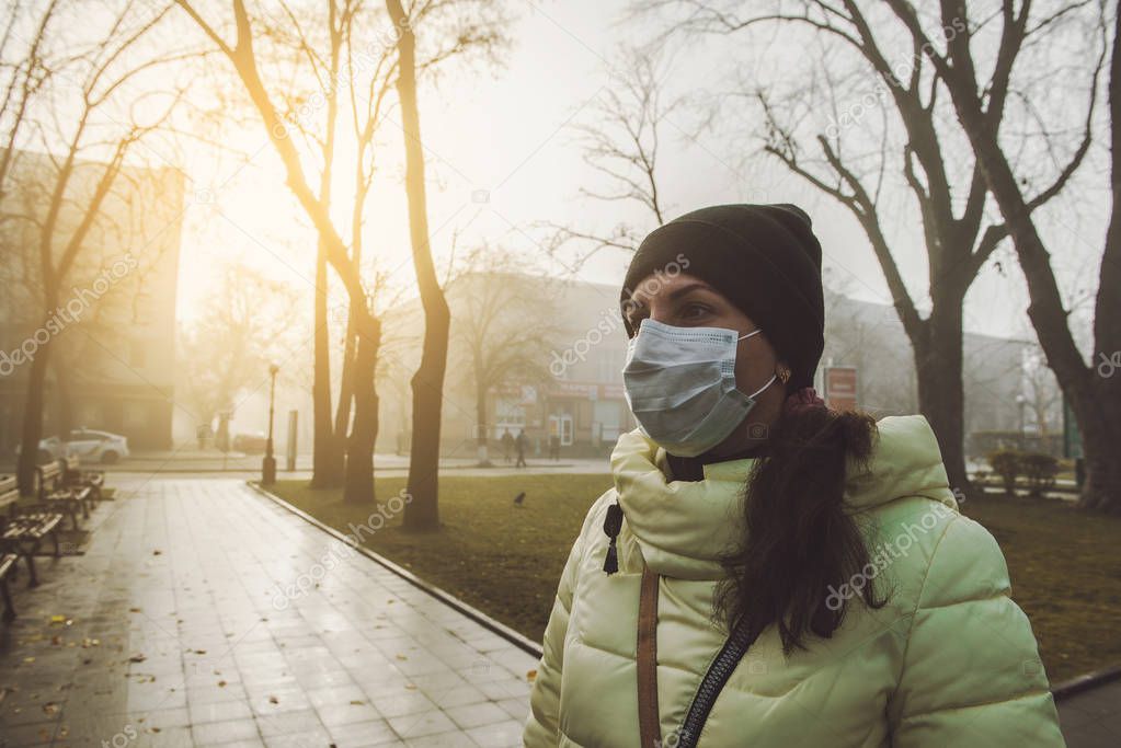 Woman suffering from sick and wearing face mask. Woman in protective mask feeling bad on the street in the city with air pollution. Smog, pollution of the environment.