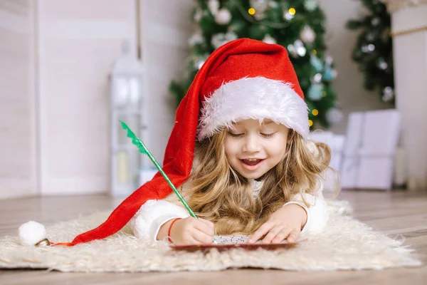 Petite fille dans le chapeau de Père Noël écrit une lettre au Père Noël — Photo