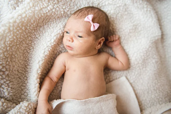 Dolce neonata con un fiocco sulla testa si trova su una coperta leggera con gli occhi aperti — Foto Stock