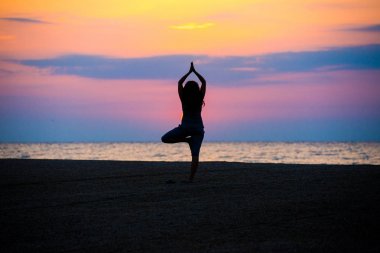 Kadın gündoğumu, deniz kıyısında yoga egzersiz yaparak