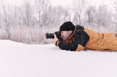 Genç adam, bir fotoğrafçı fotoğraf kamera orman arka plan bulanık kış güneşli günde içinde çeker,