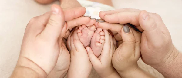 Los pies del bebé en las manos del niño mayor y de la madre —  Fotos de Stock