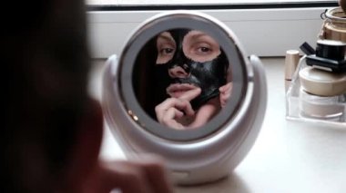 Bir kadın profesyonel kozmetik siyah bir maske kullanarak yüz cilt sonra görünüyor. Cilt temizliği, siyah bir maske ile gözenekleri. Avrupa, beyaz modeli 30-35 yıl.