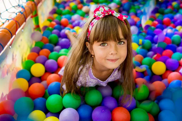 Niña feliz sentada en bolas coloridas — Foto de Stock