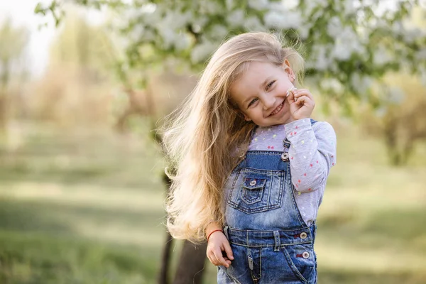 Linda niña está oliendo flores en flor en un parque de primavera . — Foto de Stock