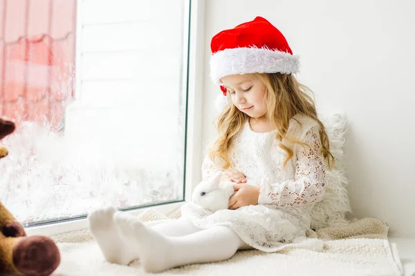 Petite fille en robe blanche avec une petite fille en robe rouge assise près de la fenêtre attendant Noël et le Père Noël — Photo