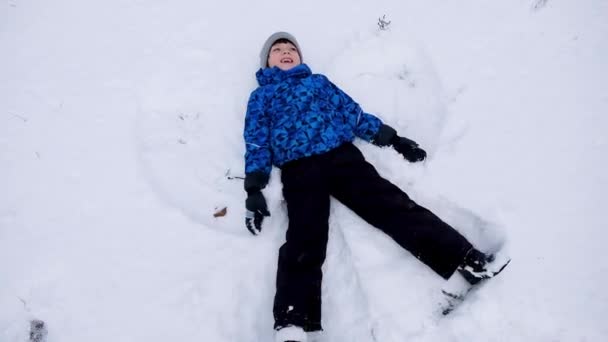 Jeux d'hiver pour enfants se trouvent dans la neige. faire un ange par un jour neigeux au ralenti — Video