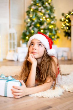 Mutlu küçük kız Noel ağacının yanında hediye kutusuyla gülümsüyor. Noel konsepti.