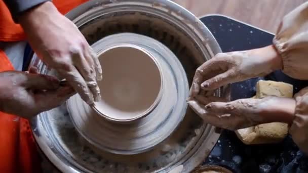 Uma lição de cerâmica. Mãos do professor e estudante em uma roda de oleiros rotativa — Vídeo de Stock