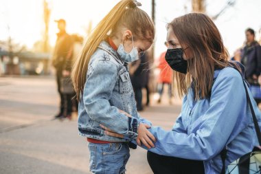 Çocuklu bir kız koruyucu bir tıbbi maskeyle yolda duruyor. Tehlikeli virüs enfeksiyonu. Avrupa 'da Coronovirüs