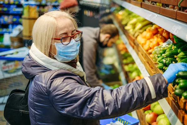 Old woman in medical masks is shopping in the supermarket looking for the food