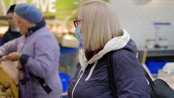 Oude vrouw met medische maskers is aan het winkelen in de supermarkt op zoek naar het eten — Stockvideo