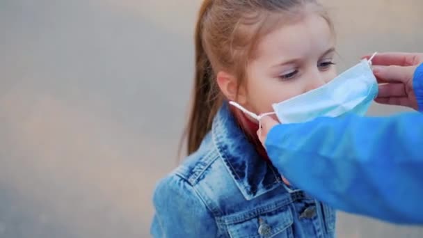 Een meisje met een kind staat op de weg met een beschermend medisch masker. Gevaarlijke virusinfectie. Coronovirus in Europa — Stockvideo