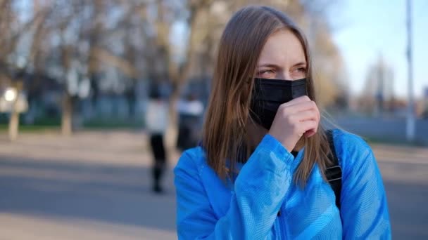 Coronavirus in Europa, infectie. Een ziek meisje staat op de weg met een beschermend medisch masker en hoesten. — Stockvideo