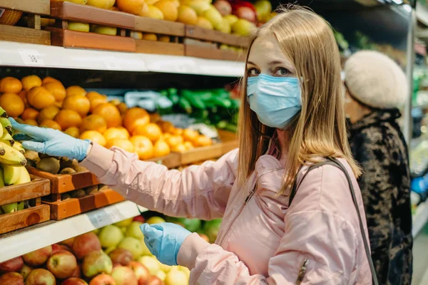 Tıp maskeli genç kız yiyecek aramak için süpermarketten alışveriş yapıyor..