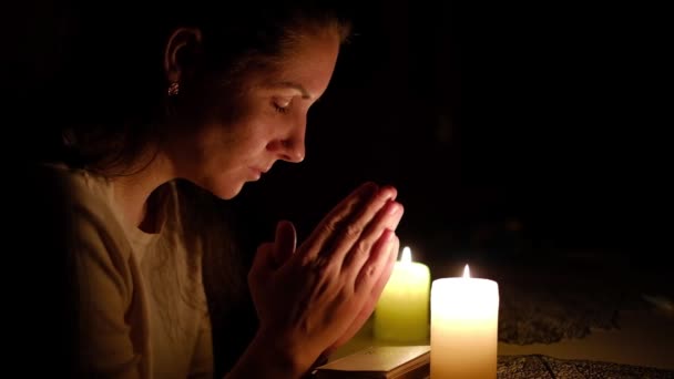 Женщина, сидящая и читающая библейские стихи при свете свечей ночью, молящаяся крупным планом — стоковое видео