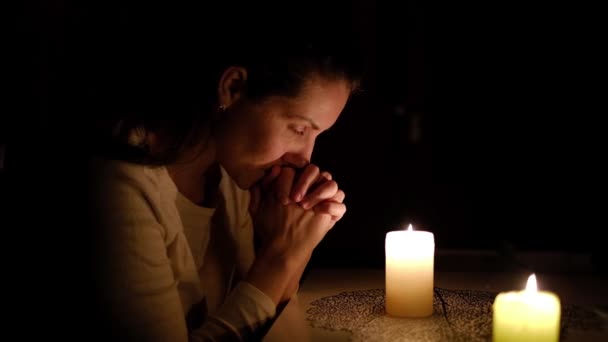 Une femme s'assoit et prie aux chandelles la nuit . — Video