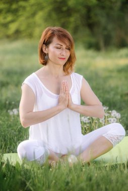 Bir kız ağacın altında meditasyon yapıyor. Doğada yoga dersleri.