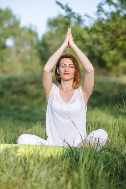 Bir kız ağacın altında meditasyon yapıyor. Doğada yoga dersleri.