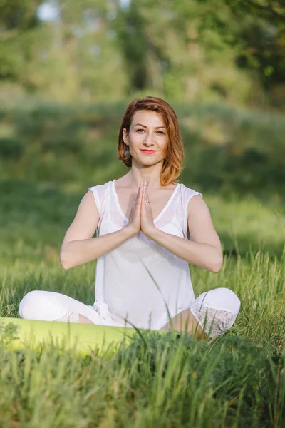 Bir kız ağacın altında meditasyon yapıyor. Doğada yoga dersleri.
