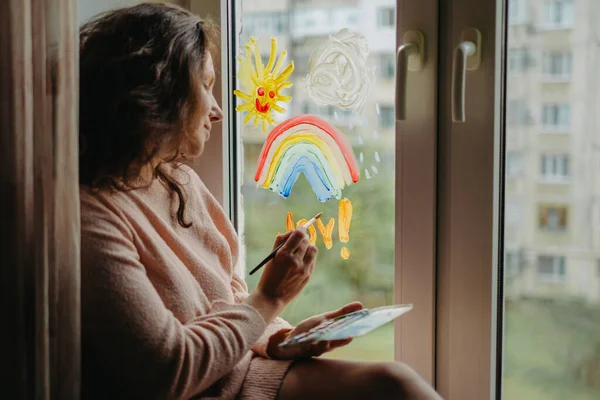 woman writes the word joy on the window
