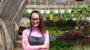 Çekici, gülümseyen bir kadın bahçıvanın portresi. Elinde çiçeklerle bir serada. Bahçe işleri, insanlar ve çiçek yetiştirme konsepti.